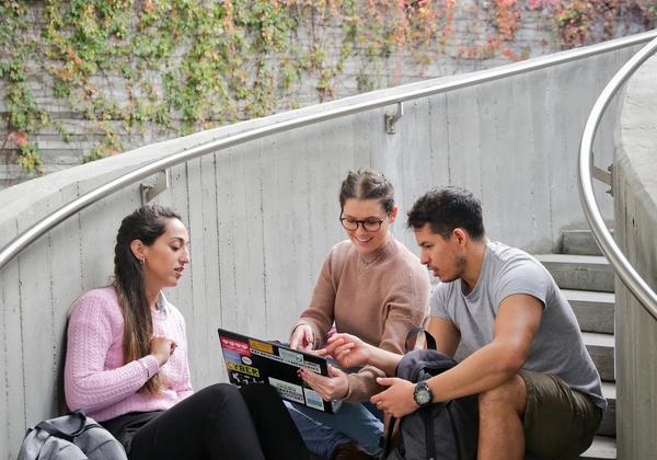 Group of 3 people sitting on outside stairs looking at a computer