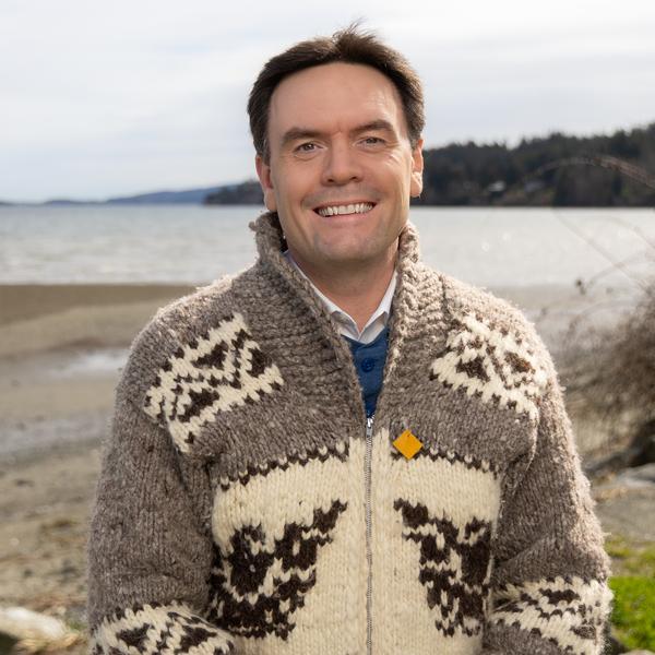 Man wearing sweater smiling with beach on backdrop